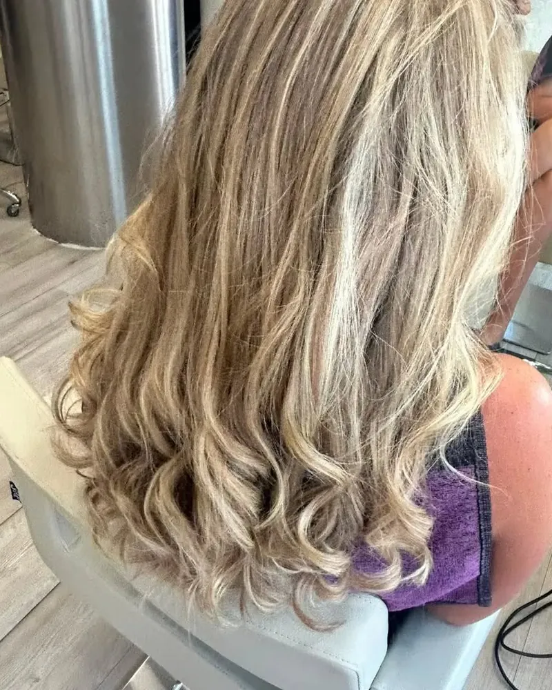 Melena rubia con ondas marcadas, vista de espaldas en un sillón del salón